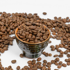 Fragrant roasted coffee beans on a white background and a small cup.