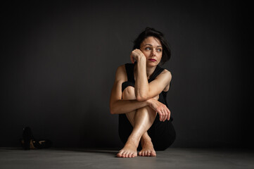 young pretty girl sitting on the floor, pensive, thinking, depression, dark background, low key