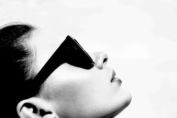 Fashion concept. Close-up woman profile portrait with sunglasses looking up and illuminated by...