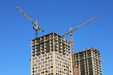 Fototapeta premium Tower cranes and unfinished buildings on background of blue sky. Housing construction, apartment blocks in city