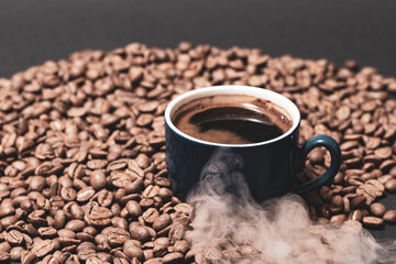 Roasted coffee and a cup of ready coffee on a dark background with light steam.