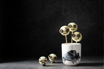 Halloween candy bar, cake pops with funny monster faces on a black background with space for text. Sweet balls in white chocolate glaze.