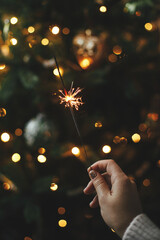 Burning sparkler in female hand on background of christmas tree lights in dark room. Happy New...