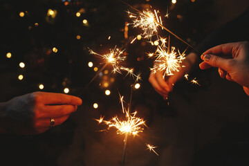 Happy New Year! Hands holding fireworks against christmas lights in dark room. Atmospheric holiday....