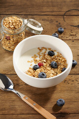 granola with yogurt and berries in a white bowl on a wooden table