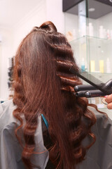 Naklejka premium hairdresser work with curling iron on light brown long hair closeup photo