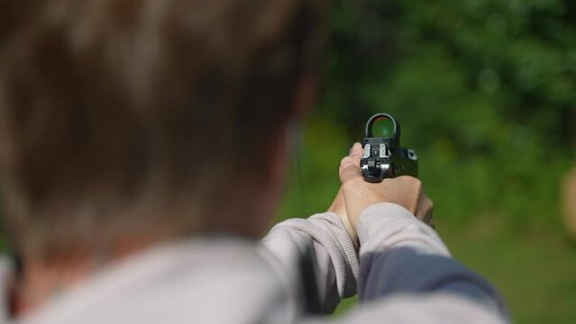 Closeup of woman firing a handgun at a target outside.