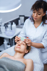 Obraz na płótnie Canvas Woman having an gua sha facial massage with natural jade stone massager in the salon