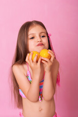 Caucasian beautiful little girl with fresh yellow lemons on a pink background.