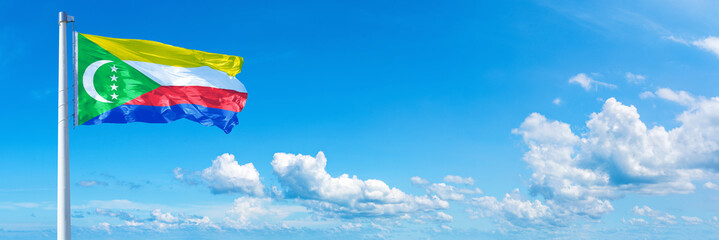 Comoros flag waving on a blue sky in beautiful clouds - Horizontal banner