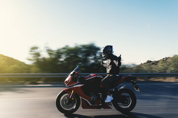 Side view of a motorcycle rider riding red race motorcycle on the highway with no hands and with...