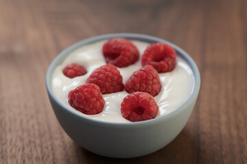 Yogurt with fresh raspberries in blue ceramic bowl on walnut table