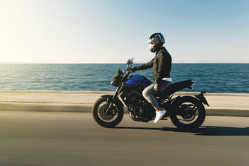 Side view of a motorcycle rider riding race motorcycle on a sea background with motion blur