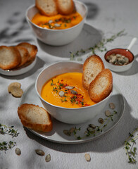 Two bowls of traditional cream pumpkin soup with thyme, pumpkin seed, red paprika and bread