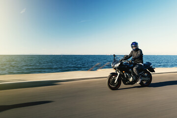 Side view of a motorcycle rider riding race motorcycle on a sea background with motion blur