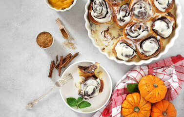 Homemade Pumpkin cinnamon rolls with cream cheese in a baking dish and a piece on the plate, flat lay, top veiw. Seasonal autumn homemade pastry - cinnabons for breakfast or holidays.