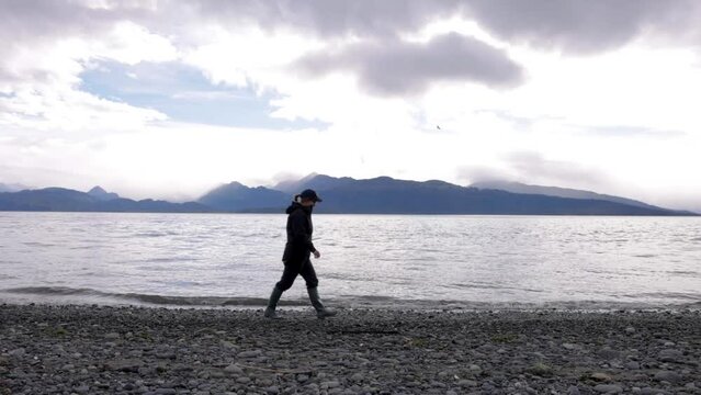 woman walking at the beach in alaska while wearing hiking outdoor wear and hiking boots during semi sunny clouydy day in homer rocky beach happy camper