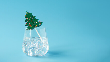 A glass with an ice drink, ice cubes and a lollipop in the shape of a Christmas tree on a light...