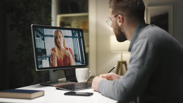 Young caucasian male in eyeglasses having videochat with felmale and making notes, preparing a project.