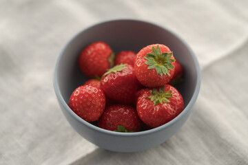 Organic ripe strawberries in blue ceramic bowl on white linen cloth