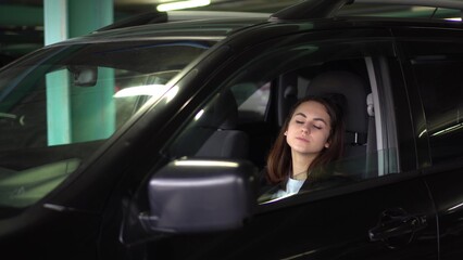 Obraz na płótnie Canvas A young solid woman sits in a car in the parking lot and falls asleep. Businesswoman in glasses and a jacket leaned back in her chair and fell asleep.