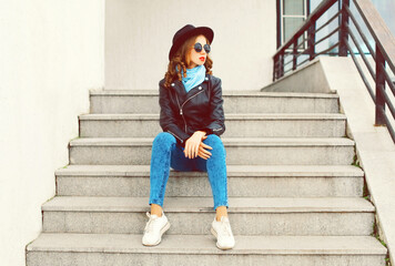 Fototapeta premium Portrait of beautiful young woman model wearing black round hat, leather jacket, sunglasses in the city street