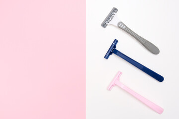 Three disposable razor blades of different colors for removing, shaving unwanted hair on face and body on white and pink background with copy space