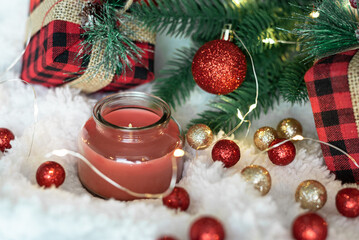 Red candle,gifts in a checkered cloth wrapper, yellow lights on a garland, a sprig of a Christmas tree on a white soft background.  Postcard for the New Year and Christmas.