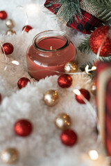 Decor of red shiny Christmas balls, gifts in a checkered package decorated with a burlap ribbon, lights of a Christmas garland on a white fluffy soft background. Cozy holidays. New Year holidays 2023.