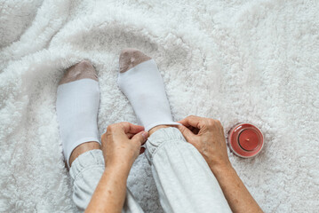 Women's hands put socks on legs sitting on a white fluffy plaid. Rest at home after a hard day's work. Varicose veins on legs. Swollen legs, problems with the bone in the legs.