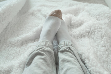 Women's legs in socks on a white fluffy plaid, at home in a cozy winter season. Relax at home. top view