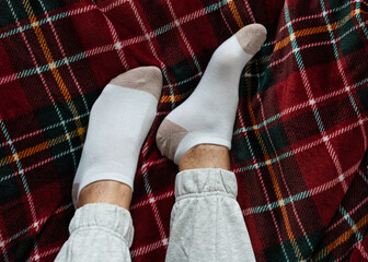 Women's legs in socks on a red checkered blanket, at home in a cozy winter season. Relax at home. Top view