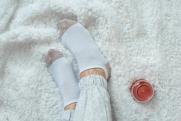 Lady's legs in socks on a white fluffy plaid, at home in a cozy autumn season. Rest at home after a hard day's work. Varicose veins on legs. Swollen legs, problems with the bone in the legs.