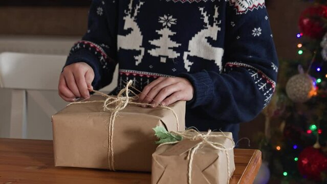 Kid in blue sweater wrapping Christmas gift with twine. 