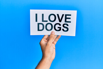 Hand of caucasian man holding paper with i love dogs message over isolated blue background