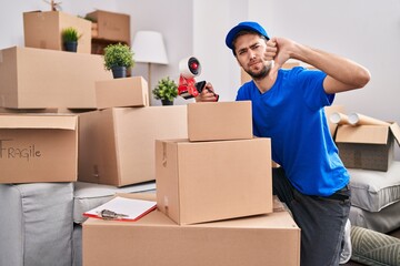 Hispanic man with beard working moving boxes with angry face, negative sign showing dislike with...