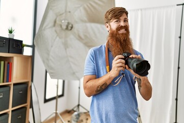 Young redhead man photographer using professional camera at photograpy studio