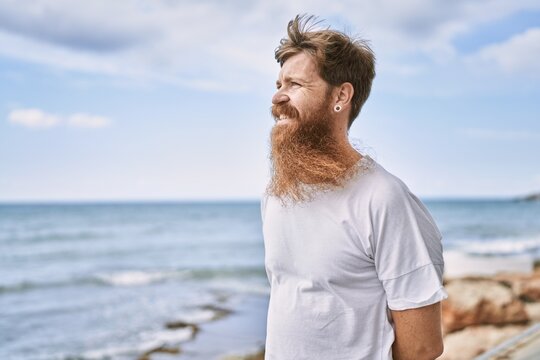 Young redhead man smiling happy standing at the beach.