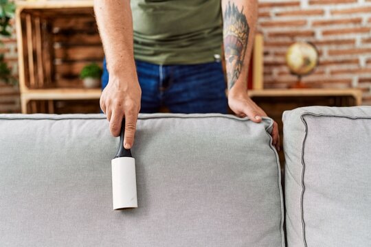 Young Redhead Man Cleaning Sofa Using Pet Hair Roller At Home