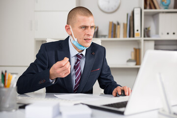 European businessman in mask having video conference on laptop in corporate modern office