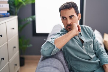 Young hispanic man sitting on sofa with serious expression at home