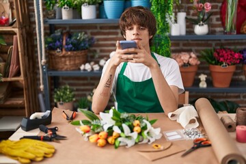 Young blond man florist make photo to flower by smartphone at flower shop