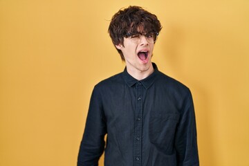Young man wearing glasses over yellow background winking looking at the camera with sexy...