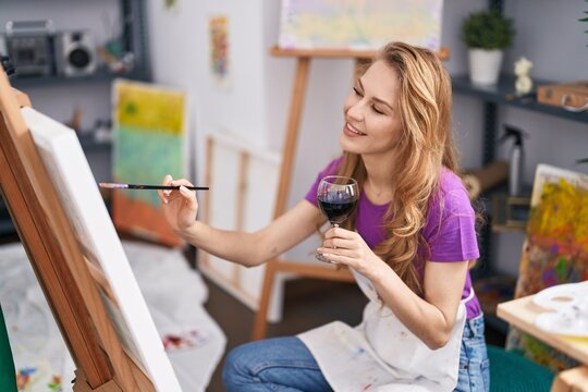 Young blonde woman artist drinking wine drawing at art studio