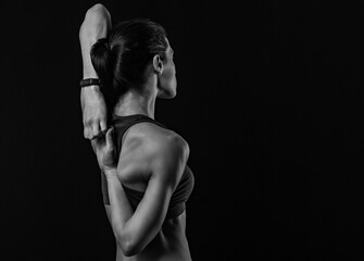 Sporty healthy body woman with strong muscular shoulders and blades doing hands the lock exercise behind the back on black studio background with empty copy space.