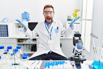 Fototapeta premium Middle age man working at scientist laboratory celebrating victory with happy smile and winner expression with raised hands