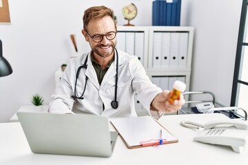 Middle age hispanic man wearing doctor uniform holding pills at clinic