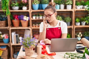 Young beautiful hispanic woman florist talking on smartphone holding gift lace at florist