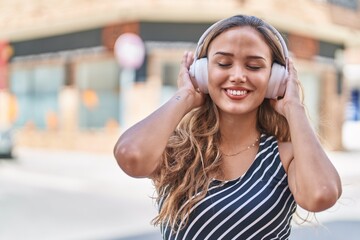 Young beautiful hispanic woman listening to music standing at street