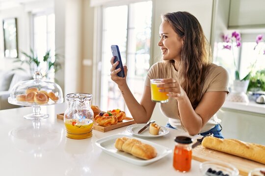 Young beautiful hispanic woman having breakfast using smartphone at the kitchen